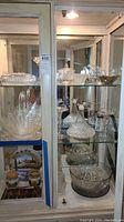 Full view of art glass collection including basket, bowls, decanter, candle holders, butter dish, creamer, and sugar bowl within glass cabinet.