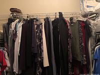 Photo of multiple women's clothing items hanging on a metal clothing rack including blouses, sweaters, pants, and jackets in various colors and styles mostly in medium size.