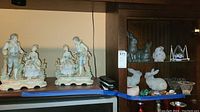 Wide view showing porcelain figurines on top shelf and rabbit figurines along with crystals and bowls on wooden cabinet shelves.