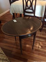Oval drop leaf table with metal drawer handle and tapered legs, showing front and top sides.