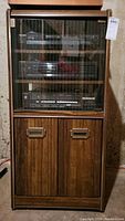 Full view of wood veneer stereo cabinet with glass door containing audio components. Cabinet has bottom-door storage section.