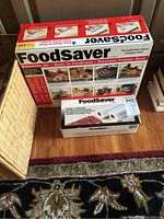 FoodSaver VAC550 vacuum sealer box and box of two rolls of VacLoc bags placed on the floor.