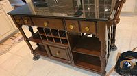 Front view of wooden kitchen island with marble top, drawers with brass knobs, wine rack and open shelves.