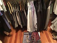 Hanging men's clothing including dress pants and shirts in a closet, with a box on floor containing various neckties