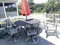 Full view of metal patio dining set on deck showing square table with umbrella hole and 6 matching chairs, 2 with swivel bases.