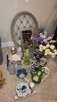 Various decorative items on floor including two mirrors, faux flowers, candles, ceramic figurines, bowls and jars