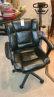 Front view of black padded office chair with cushioned seat and backrest, armrests, caster wheels, and adjustable height mechanism.