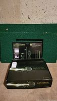 Main closed Optishot Infrared Golf Simulator box on green mat and concrete floor with a getting started guide behind it.