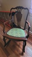 Full view of wooden rocking chair with upholstered seat showing carved backrest and curved armrests.