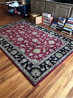 Full view of the red and black floral patterned area rug on hardwood flooring, showing overall condition and design details.