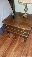 Front view of Kling Colonial solid cherry side table with lamp and clock on top, showing drawer fronts and turned legs on hardwood floor.