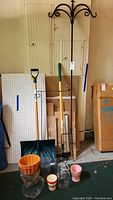 Snow shovel, shepherds hooks, garden edger, various pots and vases arranged on garage floor.