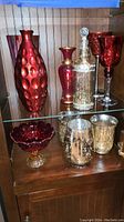 Shelf display showing all 8 pieces together including red textured vase, smaller red vase, amberina candy bowl, mercury glass decanter, two mercury glass votives, red wine glass and tall multicolor vase.