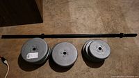 Photo of barbell bar and two sets of metal weight plates arranged on floor