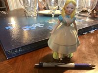 Front view of Alice In Wonderland ceramic figurine on tabletop with pen for scale