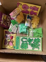 Box containing various character and holiday-themed cookie cutters including Simpsons, Sesame Street, Teenage Mutant Ninja Turtles, Barney, Easter, Dinosaurs, and St. Patrick's Day shapes