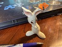 Front view of the white porcelain rabbit figurine with orange butterfly on its ear next to a pen for scale.
