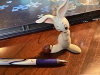 Front view of white porcelain rabbit with small hedgehog figurine and pen for scale on wooden surface.