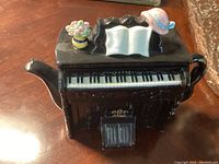 Front view showing black piano shape with keyboard and decorative lid with hat and flowers