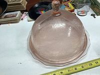 Pink Depression glass cake dome and plate set shown on tabletop with ruler for size reference, no chips or cracks visible.
