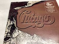 Front album cover for Chicago X vinyl record showing embossed logo with wear and tear including torn top edge.