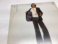 Front cover of James Taylor "In The Pocket" album jacket showing James Taylor wearing a black suit jacket and pants, standing forward with a white t-shirt underneath.