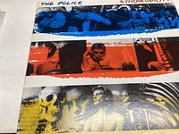 Close-up photo showing colorful strip artwork on the album cover with band members and clocks in blue, red and yellow tones.