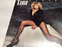 Close-up of Tina Turner album cover showing Tina sitting with black outfit and fishnet stockings on dark background.
