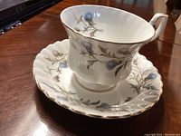 Tea cup and saucer set showing floral pattern and gold trim on a wooden table.