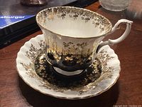 Close-up of tea cup and saucer showing gold designs and ornate handle
