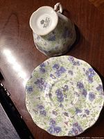 Underside of the tea cup displaying the Royal Albert hallmark logo and pattern name on white porcelain, resting on a wooden surface.
