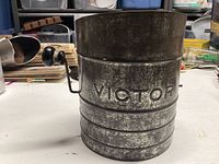Side view of Victor metal flour sifter showing embossed brand and textured surface.