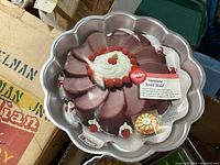 Top view of the Wilton Viennese Swirl Cake Pan with packaging showing cake example and product label.