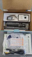 Camera with original box containing camera, tripod, USB cable, software CD, manuals, and memory card.