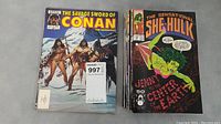 Stack of comic books including visible covers of The Savage Sword of Conan and She Hulk.