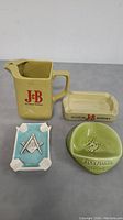 Overview of all four items: J&B pitcher, J&B rectangular ashtray, Remy Martin Cognac round ashtray, Masonic ashtray.