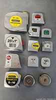 Top view of all 13 tape measures showing brand labels, sizes, and metal casing condition
