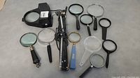 Lot of eleven magnifying glasses of various sizes and types including vintage models lying flat on a surface.
