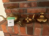 Brass kettle, small elephant figurine, chamberstick candle holder, small vase on brick background