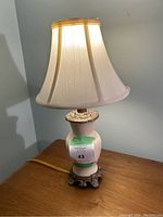 Full view of assembled table lamp with cream shade on top of wooden table, base has crackle glaze ceramic vase and decorative dragon style mount at bottom