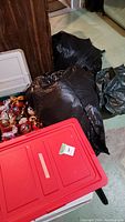 Black bags containing artificial Christmas trees alongside red and white storage bins