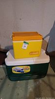 Stacked view showing smaller yellow TrinaPacker cooler on top of larger green Cooler 85 Combo cooler.