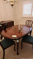 Dark wood dining table with curved edges and classic legs, accompanied by three chairs and two candlesticks on top. The table surface appears well maintained with minor wear.
