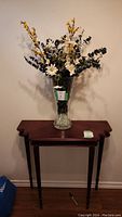 Entry display table with dark wood veneer finish shown against a plain wall with decorative flowers on top.