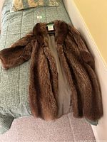 Full view of a brown fur jacket laid on a bed showing its fur texture and lining.