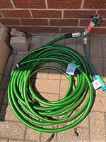 Photo of the long green garden hose coiled on ground with spray nozzle and splitter valve attached, placed on outdoor brick patio