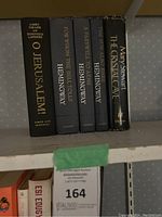 Photo of six hardcover books including Hemingway and Mary Stewart on a shelf with lots label visible