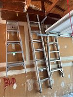 Three metal ladders hanging on a garage wall, including one long extension ladder and two smaller step ladders.
