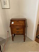 Mini wooden secretary desk in corner, showcasing fold-down writing surface, drawer, and overall design.