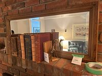 Mirror mounted on a brick wall reflecting old books and a small giraffe statue